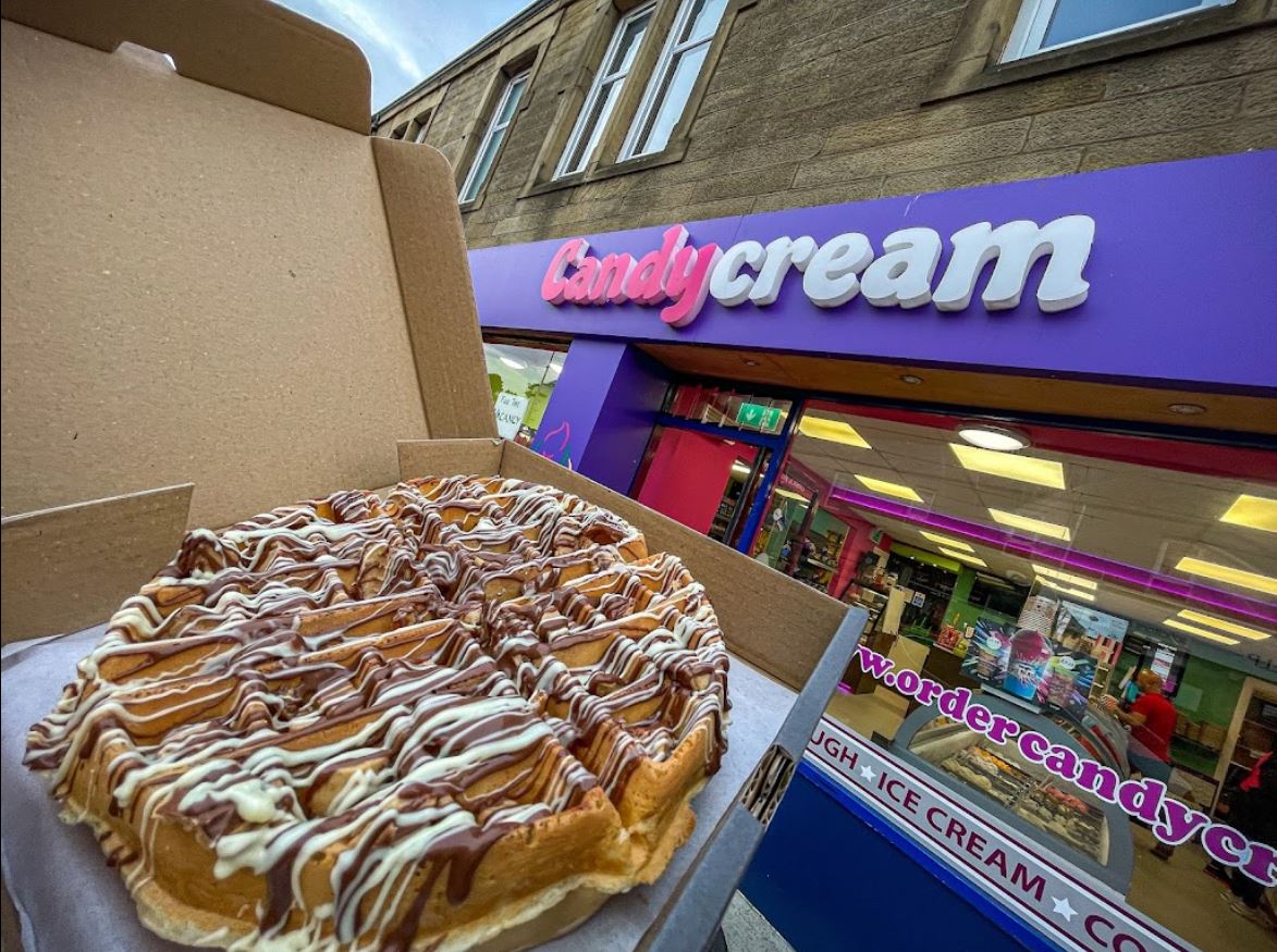 Fresh golden waffle drizzled with chocolate sauce, held in front of the Candy Cream 
dessert shop in Bathgate 
