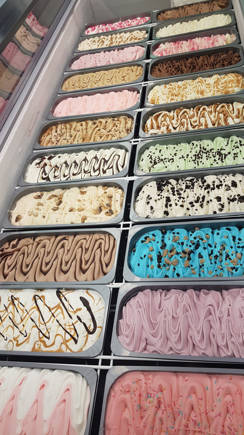 Display case showcasing multiple tubs of colourful artisan ice cream and gelato 
flavours at Candy Cream shop in Bathgate