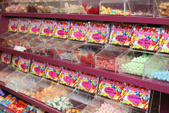 view of the self-serve Pick 'n' Mix wall at Candy Cream Bathgate, showing colourful 
bulk candy, jelly sweets, and bubblegum in clear bins with price labels