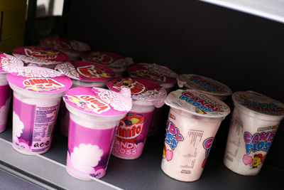 Shelf display of brightly packaged pink tubs of JimJam Candy Floss, a grab-and-go 
sweet product available at Candy Cream Bathgate